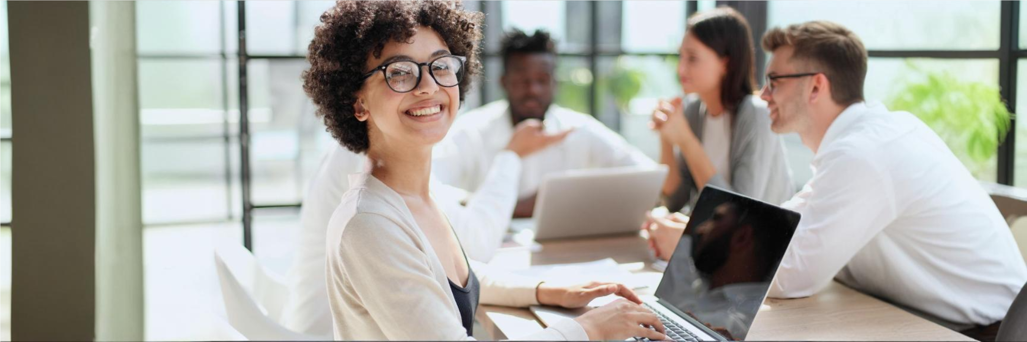 Jovem contadora negra e com cabelo cacheado sorridente para a foto durante reunião com colegas